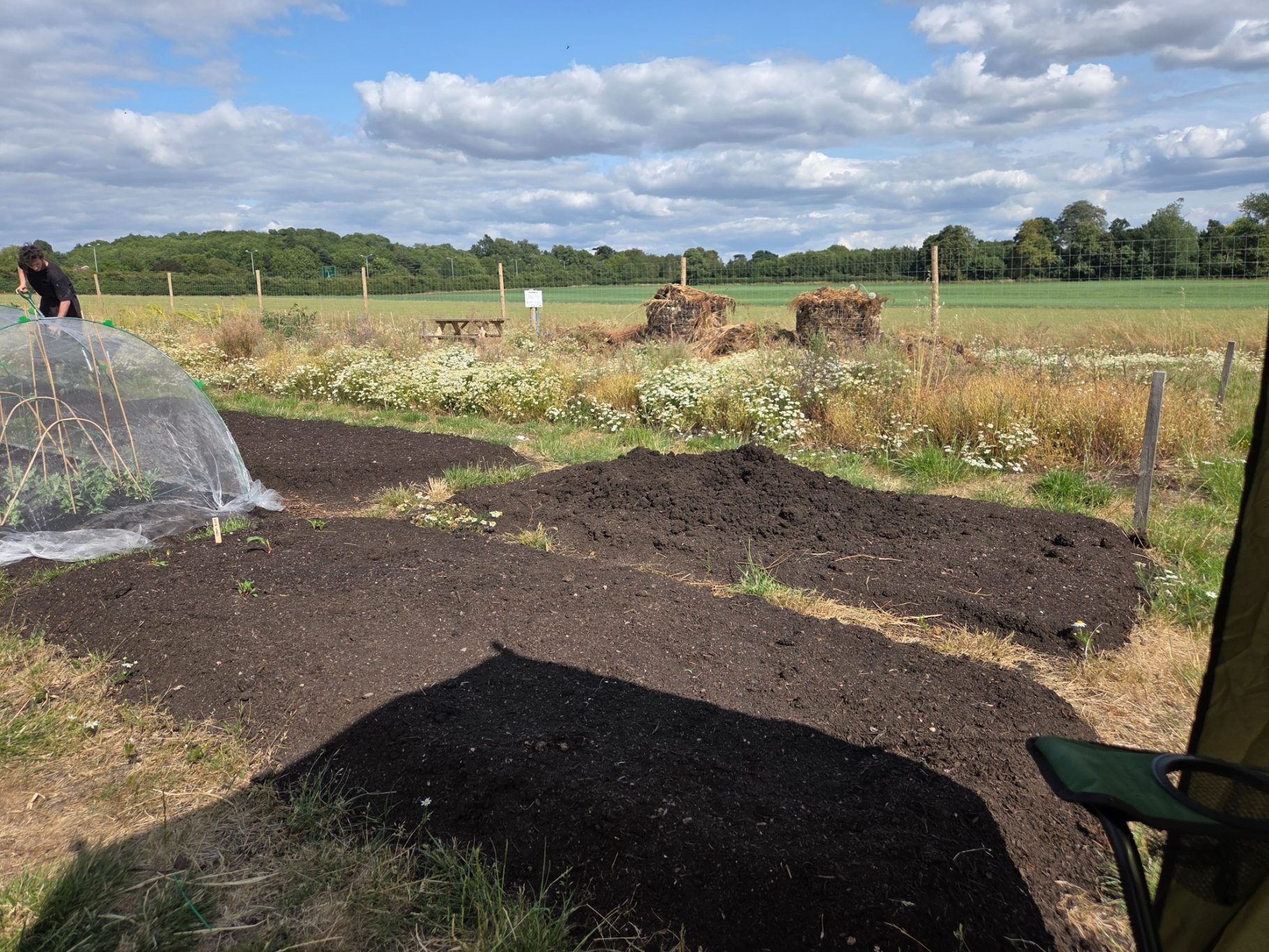 A view of freshly turned soil in a rural garden, with fields and trees in the background.