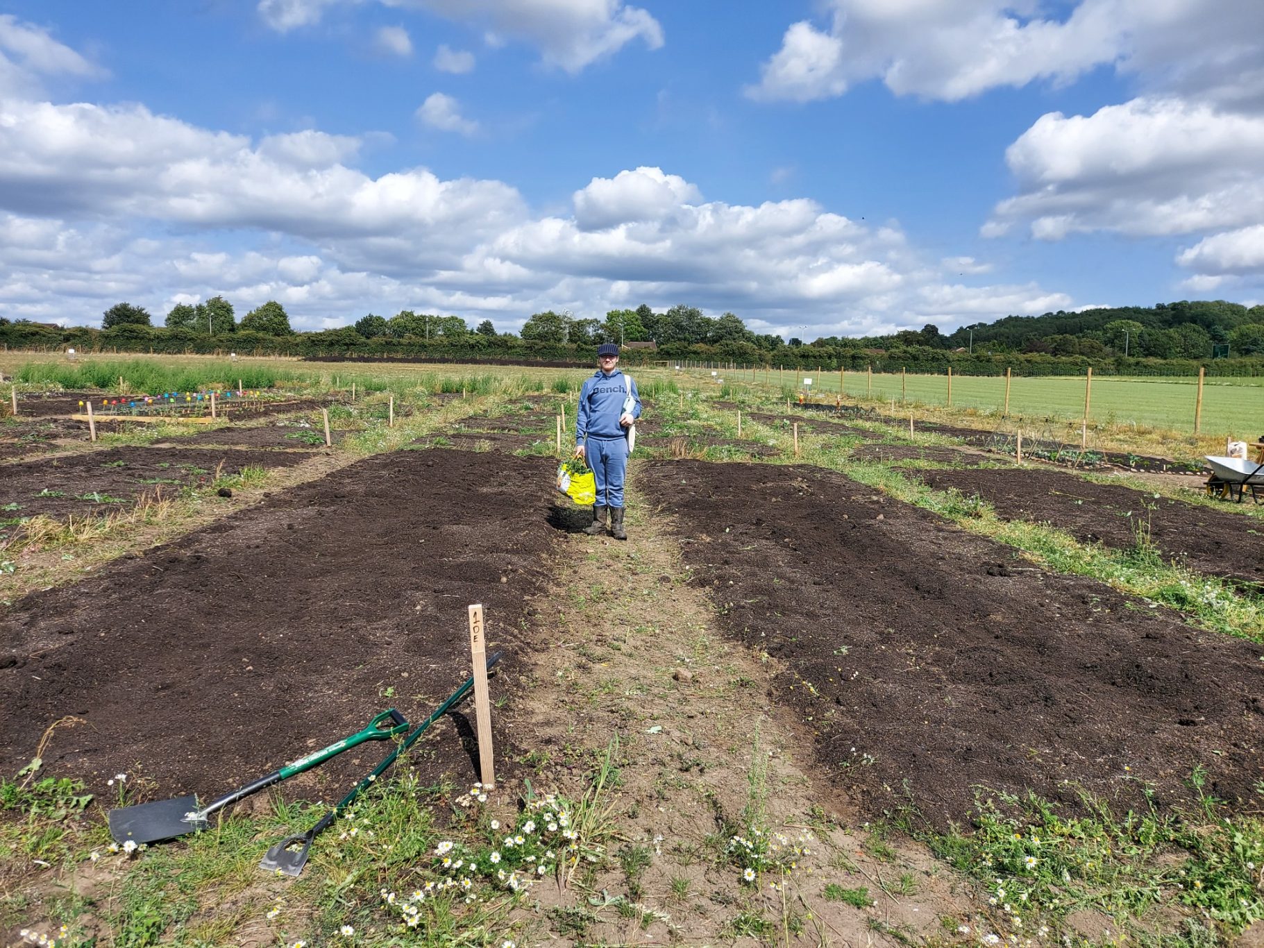 Person pushing a wheelbarrow through a vast, freshly tilled field under a blue sky.