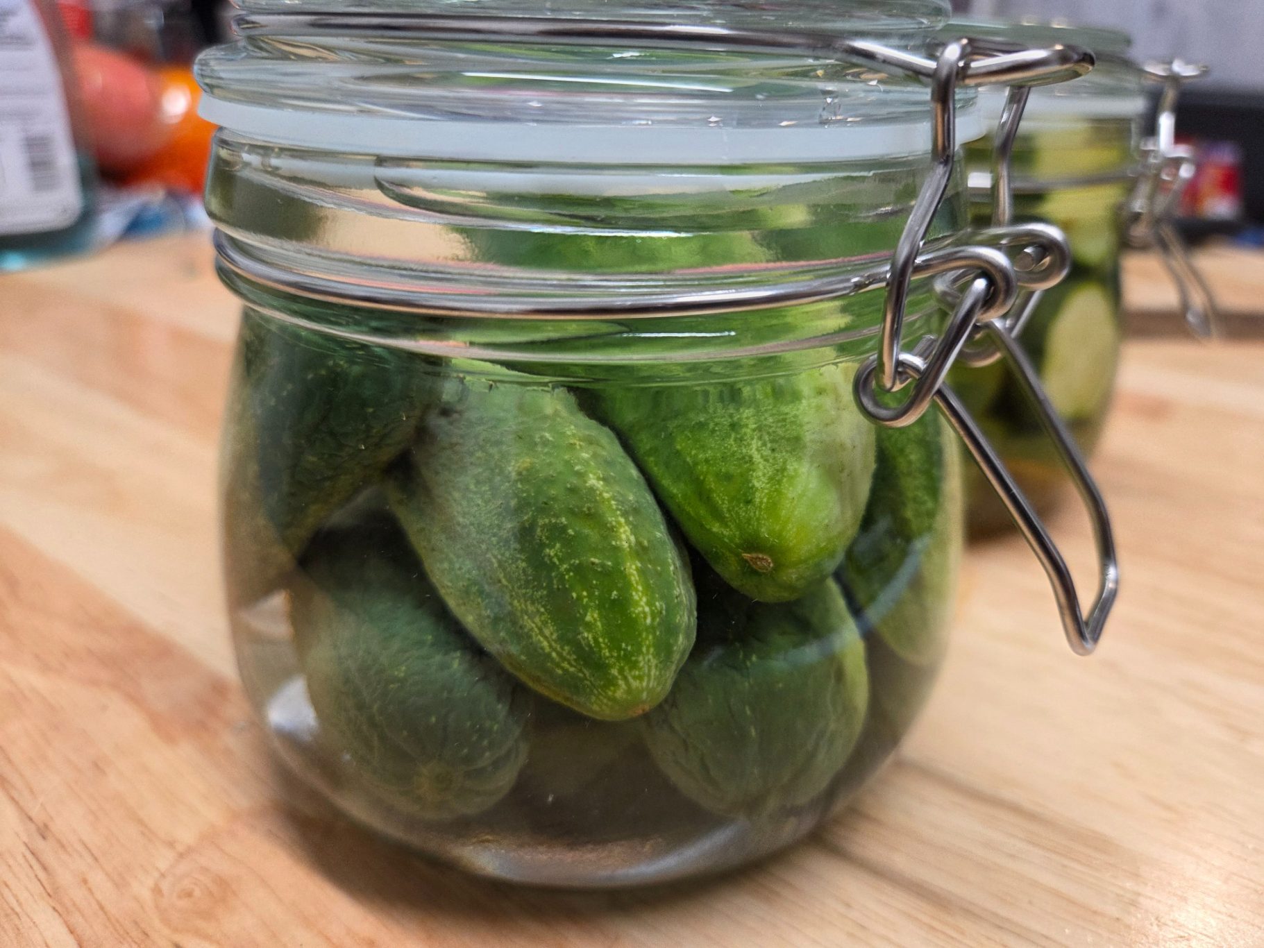 Jar filled with small, fresh cucumbers on a wooden surface.
