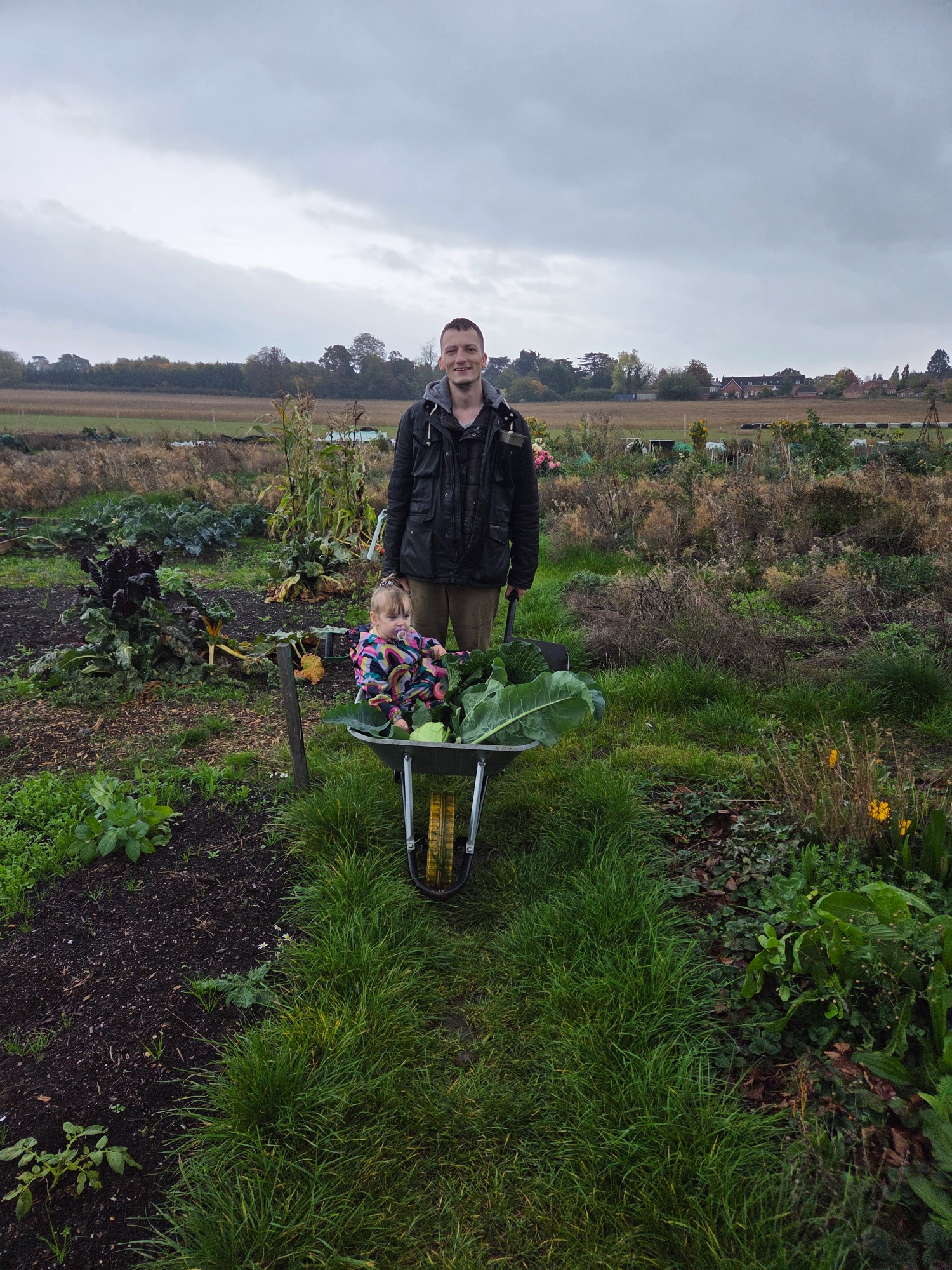 Navigating the mess dangerous to children Person standing next to a wheelbarrow in a garden with plants and a cloudy sky.