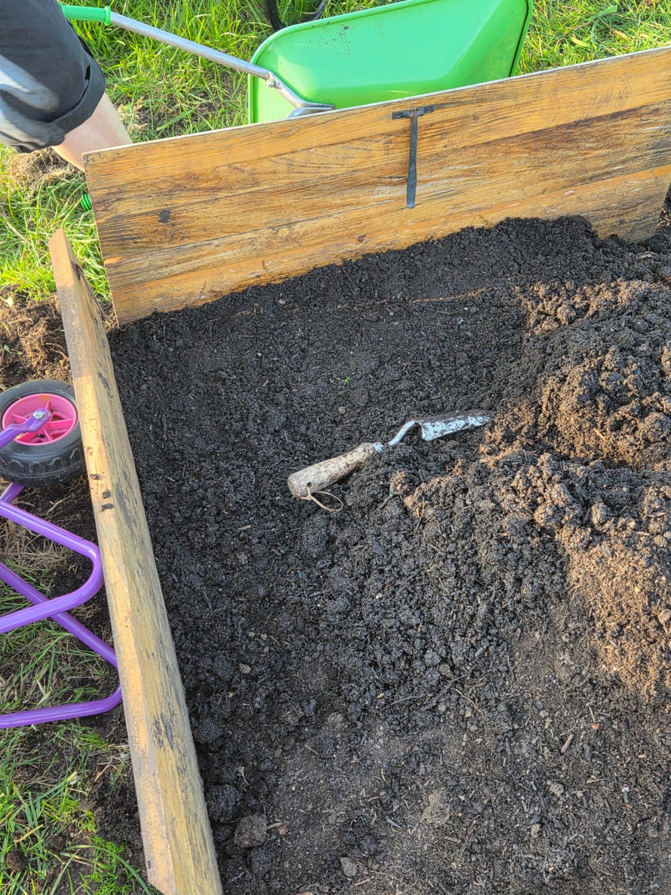 Hand trowel resting on freshly turned soil in a wooden garden bed.