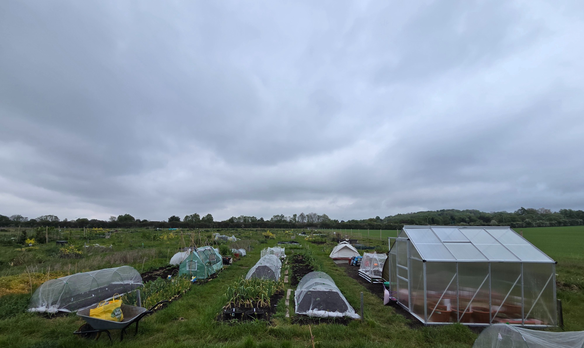 Looking amazing A panoramic view of an agricultural field with greenhouses and garden plots under a cloudy sky.